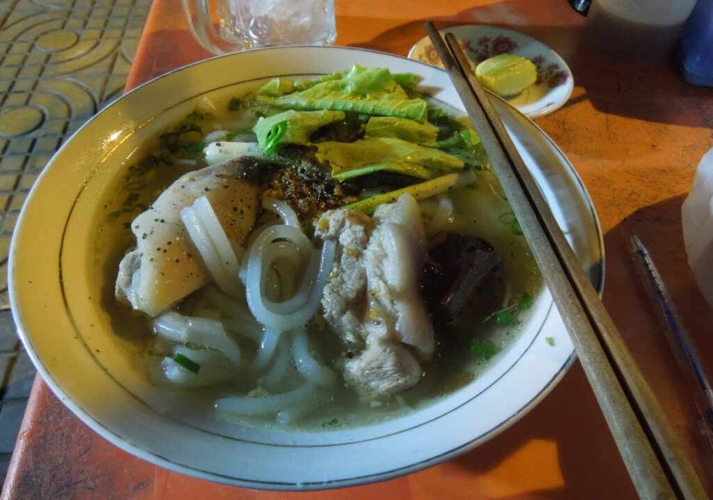 Tô bánh canh thịt heo, rau xanh ăn kèm chanh trên bàn quán vỉa hè