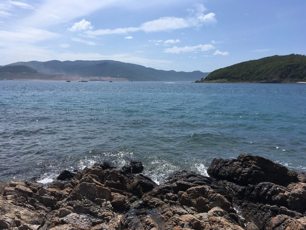 Mặt vịnh Nha Trang lấp lánh nắng nhìn từ bờ đá Hòn Miễu, tàu thuyền xa xa