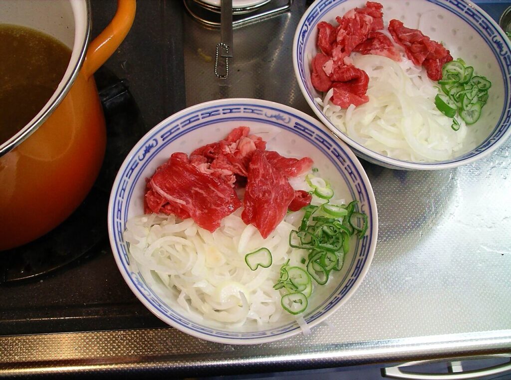 Thịt bò tái xếp trên bánh phở cạnh nồi nước dùng đang sôi