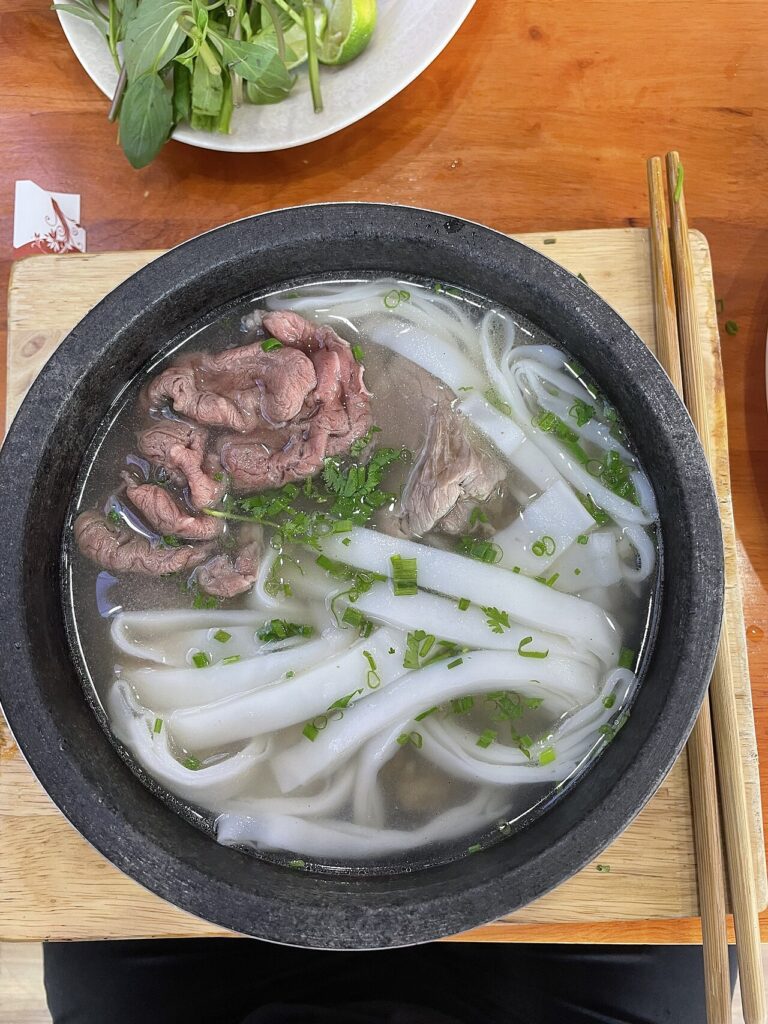 Phở bò thố đá với thịt bò tái, sợi phở bản to và hành lá