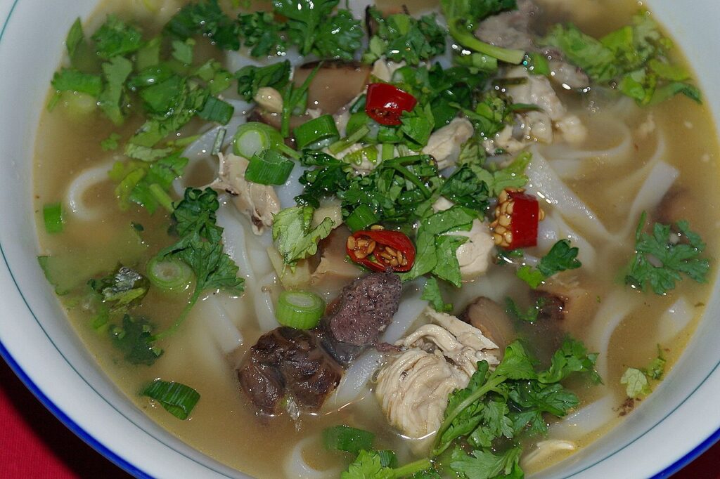 Tô phở gà ta với thịt gà xé, rau mùi, ớt đỏ và sợi phở bản to