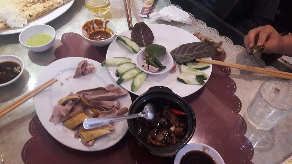 Bàn tiệc dê với thịt dê hấp, lá cuốn, dưa leo và chén nước chấm
