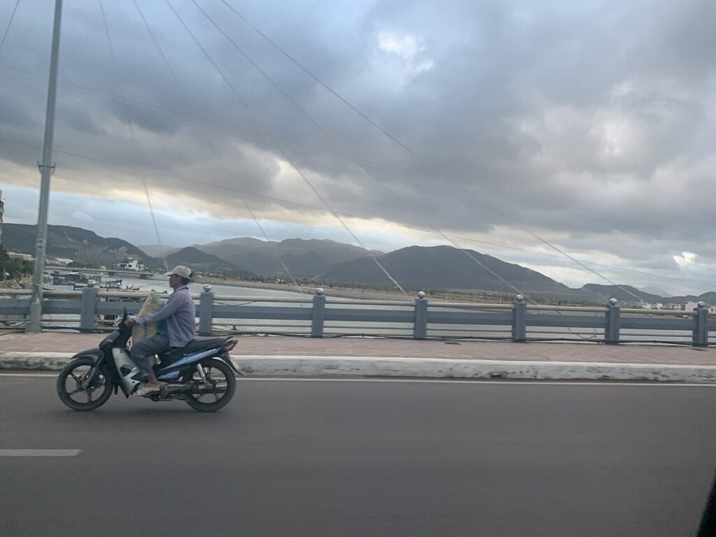 Chạy xe máy qua cầu ở Nha Trang, phía xa là núi